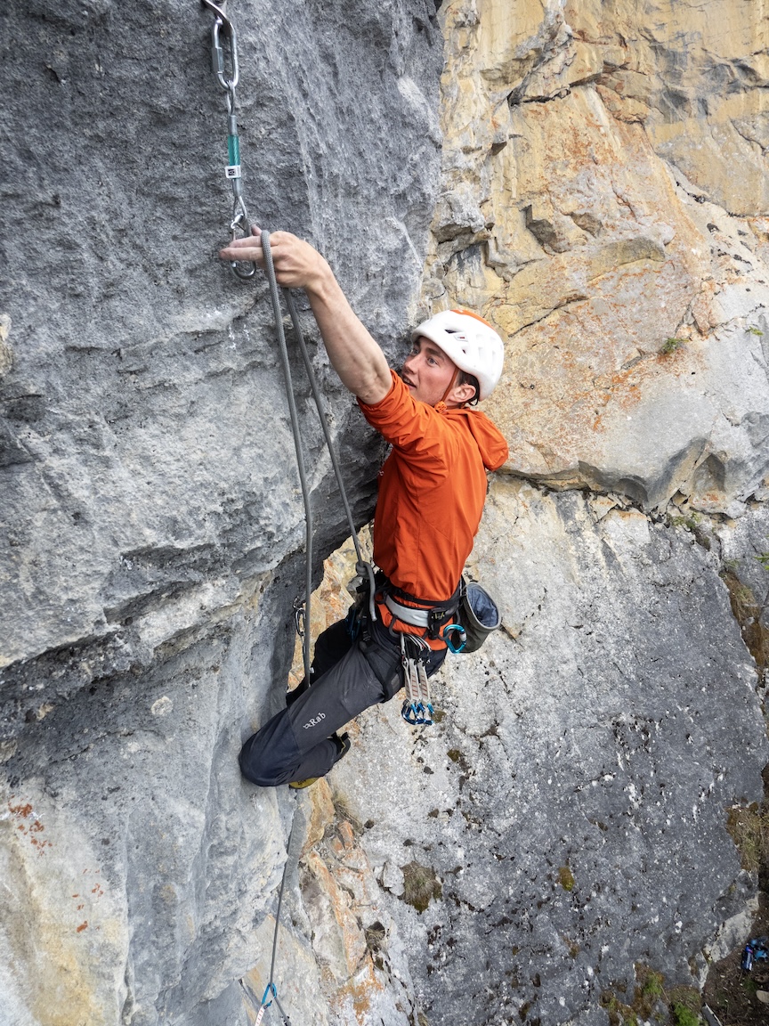 Climber reaching to clip into a perma draw.