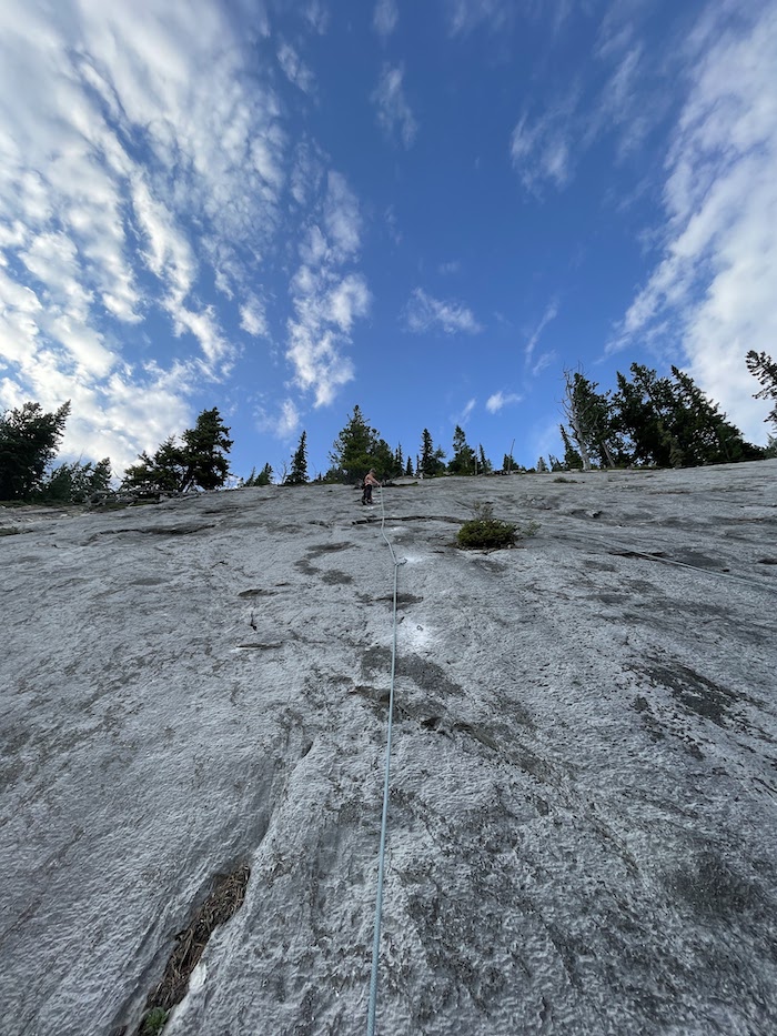 Climber is high up on a slab slope showing freshly drilled bolts.