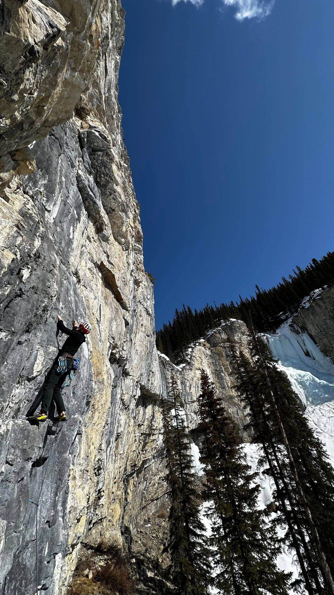 Climber is ascending a route while the ground and opposite wall are covered in snow.