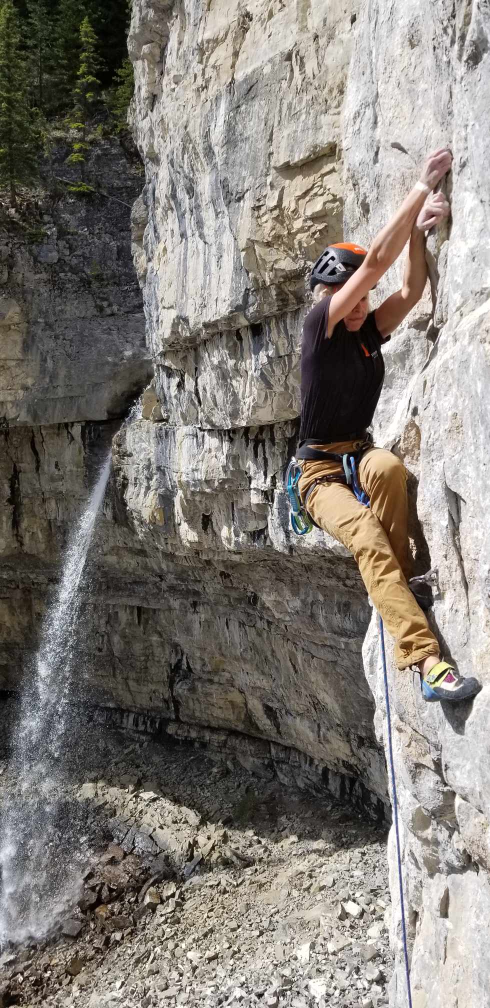 A climber works a route while a waterfall is seen in the background.